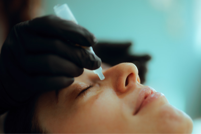 Close-up of a woman receiving a nasal peptide treatment, administered by a gloved practitioner.